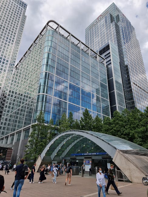 The image showcases a modern cityscape with a prominent glass-fronted office building reflecting the cloudy sky, situated amidst other tall commercial skyscrapers. In the foreground, a busy outdoor pl